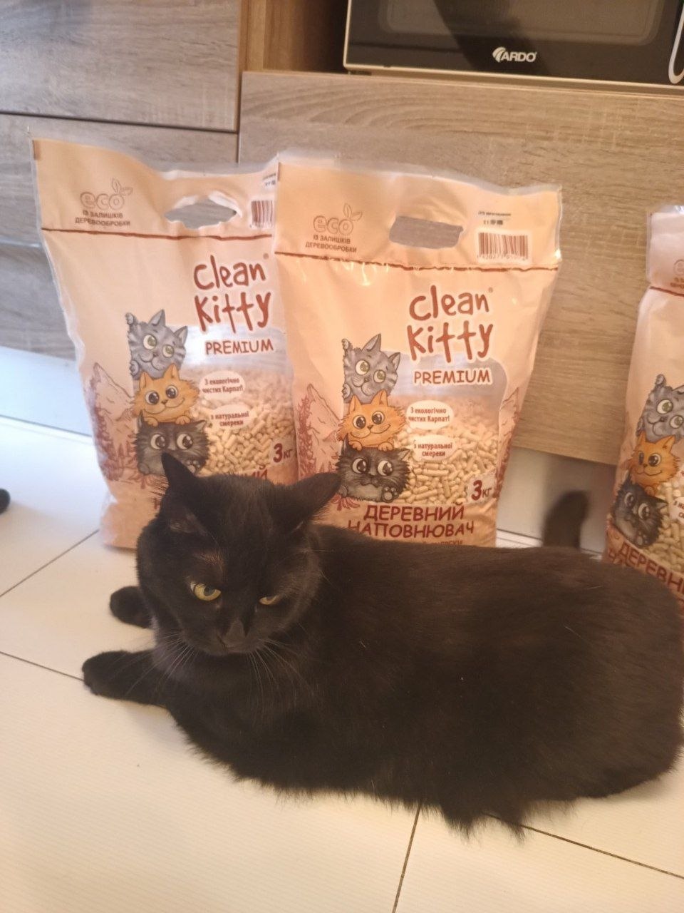 Un gatto nero sdraiato in cucina davanti ai sacchi di Clean Kitty PREMIUM